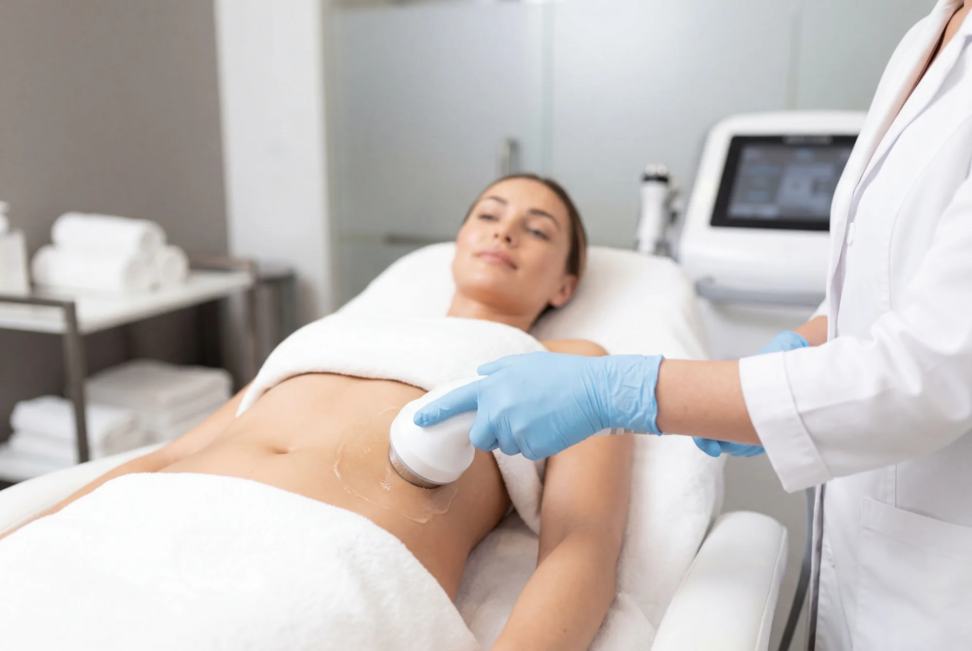 Gloved practitioner performing an ultrasound cavitation treatment on a woman's abdomen
